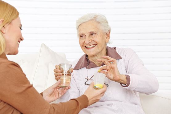 Fröhliche Seniorin mit Pflegekraft während der Medikamenteneinnahme bei der ambulanten Pflege